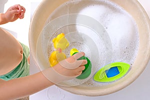 happy child, girl 3 years old plays with rubber green, yellow ducks for swimming, plastic boat, child's toys in soapy foam,