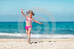 Happy child girl in bikini running on beach in summer sea