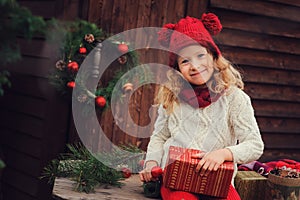 Happy child girl celebrating christmas outdoor at cozy wooden country house with gifts