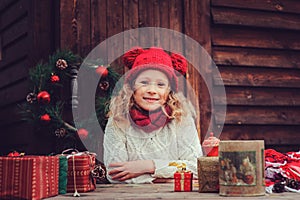 Happy child girl celebrating christmas outdoor at cozy wooden country house with gifts