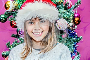 Happy child girl in a Christmas hat standing in the front of Christmas tree