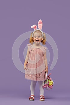 Happy child girl in costume Easter bunny rabbit with ears and a basket with eggs. Little girl on a purple