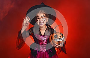 Happy child girl in costumes of witch  in dark red background in halloween