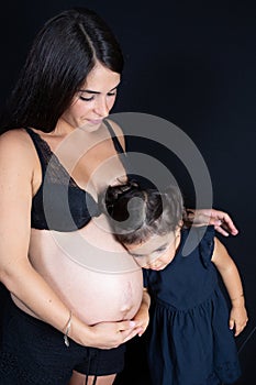 Happy child girl daughter holding belly of pregnant woman mother