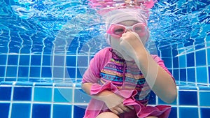 Happy child girl diving underwater in swimming pool. Family summer vacation.