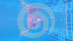 Happy child girl diving underwater in swimming pool. Family summer vacation.