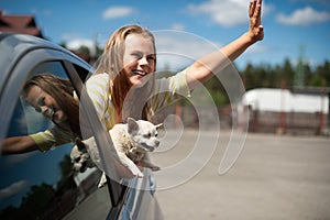 Happy child girl and dog chihuahua looking out the open car window