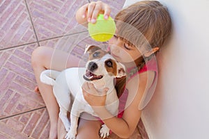 Happy child girl and dog playing with ball together