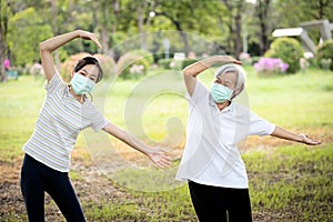 Happy child girl is doing exercise activity for the old elderly,healthy senior woman workout and wear face mask outside home after