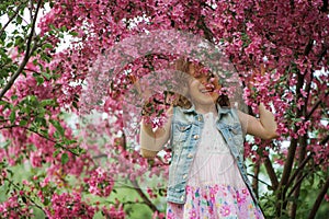 Happy child girl in dress playing near blooming tree in spring garden.