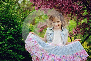 Happy child girl in dress playing near blooming tree in spring garden.