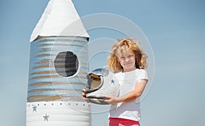 Happy child girl dressed in an astronaut costume playing with hand made rocket. Summer outdoor