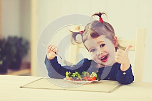 Happy child girl eat vegetables and showing thumbs up