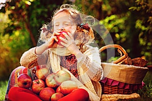 Happy child girl eating apples in autumn garden