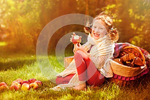 Happy child girl eating apples in autumn sunny garden