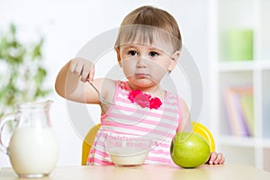 Happy child girl eating food itself with spoon