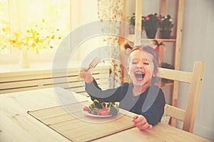 Happy child girl eating vegetables and laughs