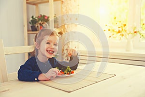 Happy child girl eating vegetables and laughs