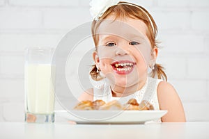 Happy child girl eats cookies and milk