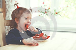 Happy child girl eats strawberries in summer home kitchen