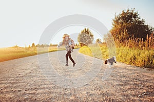 Happy child girl enjoying summer vacations with her dog, walking and playing on sunny meadow