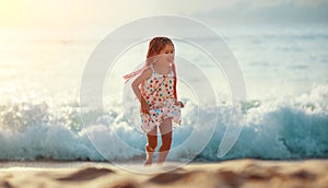 Happy child girl with flying hair dancing and runing on beach at sunset