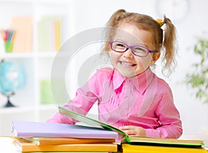 Happy child girl in glasses reading books in room