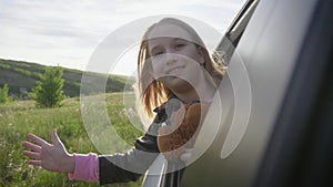 Happy child girl goes to summer travel trip in the car. Summer road trip concept. Little fun girl speeds in car near the