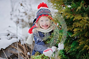 Happy child girl in hat with christmas ornament in winter garden