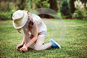 Happy child girl in hat enjoying warm summer day in the blooming garden