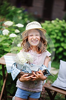 Happy child girl in hat enjoying warm summer day in the blooming garden