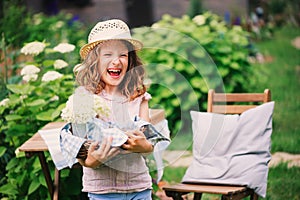 Happy child girl in hat enjoying warm summer day in the blooming garden