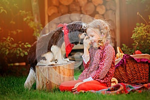 Happy child girl having fun playing with her dog in sunny autumn garden