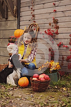 Happy child girl and her dog picking fresh apples on the farm. Country living concept