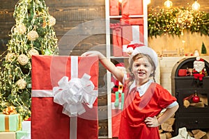 Happy child girl holding a big red gift box. Kid having fun near Christmas tree indoors. Winter delivery service for