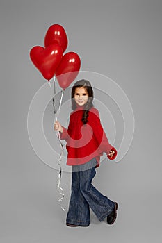 Happy child girl holding red heart shaped balloon