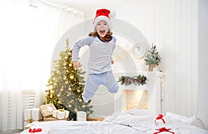 Happy child girl jumping in bed on Christmas morning