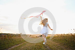 happy child girl with a kite running on meadow in summer in nature