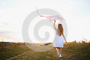 happy child girl with a kite running on meadow in summer in nature