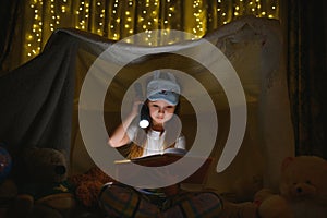 happy child girl laughing and reading book in dark in a tent at home.