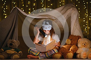 happy child girl laughing and reading book in dark in a tent at home.