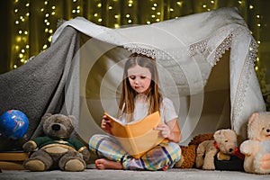 happy child girl laughing and reading book in dark in a tent at home.