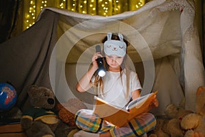 happy child girl laughing and reading book in dark in a tent at home.