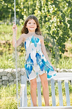 Happy child girl laughing and swinging on a swing at summer garden. Little girl having fun on a swing outdoor. Little