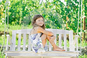 Happy child girl laughing and swinging on a swing at summer garden. Little girl having fun on a swing outdoor. Summer