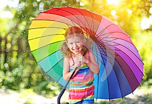 Happy child girl laughs and plays under summer rain with an umbrella.