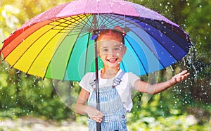 Happy child girl laughs and plays under summer rain with an umbrella.