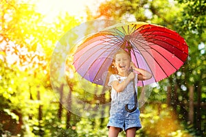 Happy child girl laughs and plays under summer rain with an umbrella photo