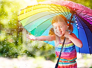 Happy child girl laughs and plays under summer rain with an umbrella. photo