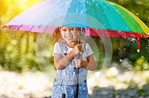 Happy child girl laughs and plays under summer rain with an umbrella.